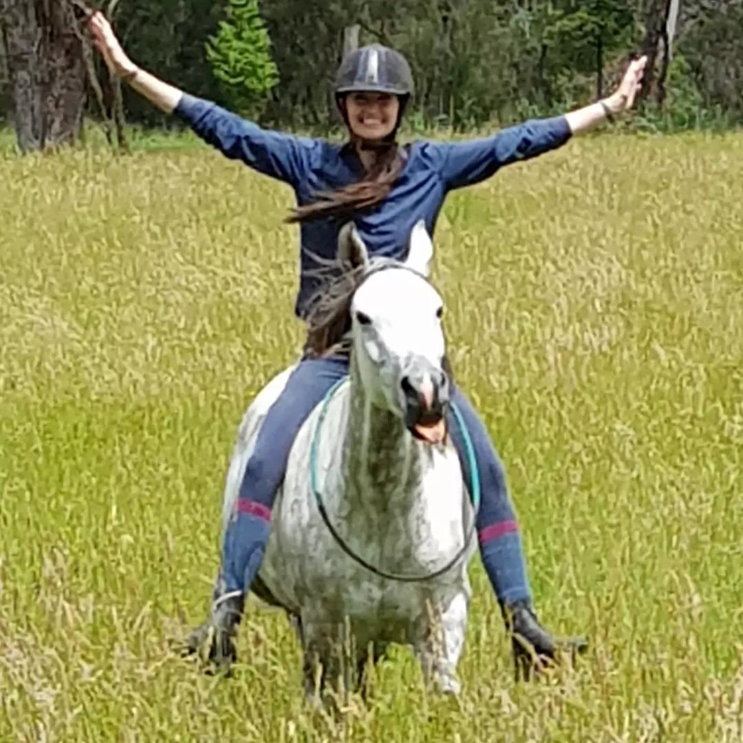 Arms outstretched riding Rahni bridleless in a green paddock